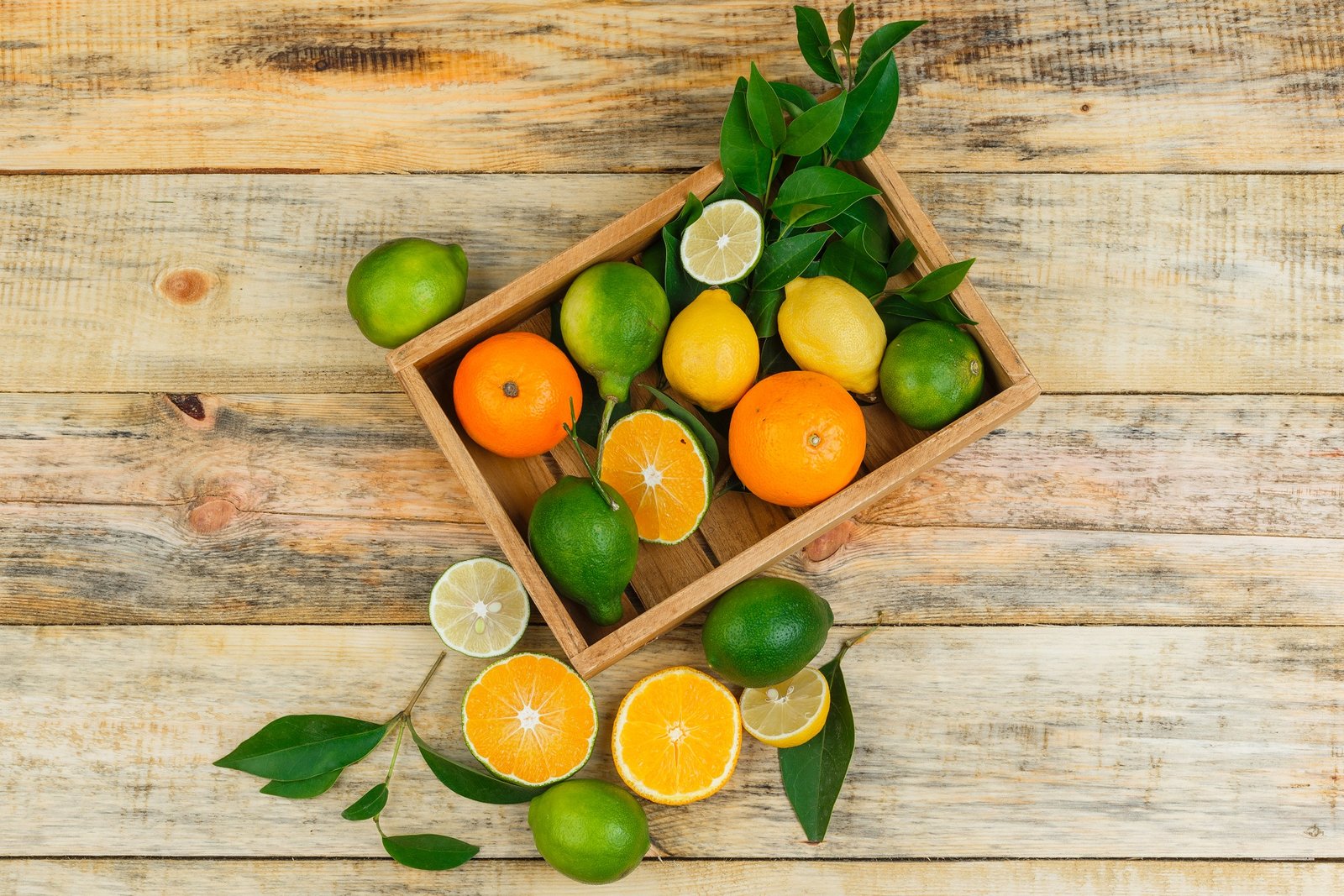 Lemons,limes and oranges in a wooden crate with leaves high angle view on a wooden board background
